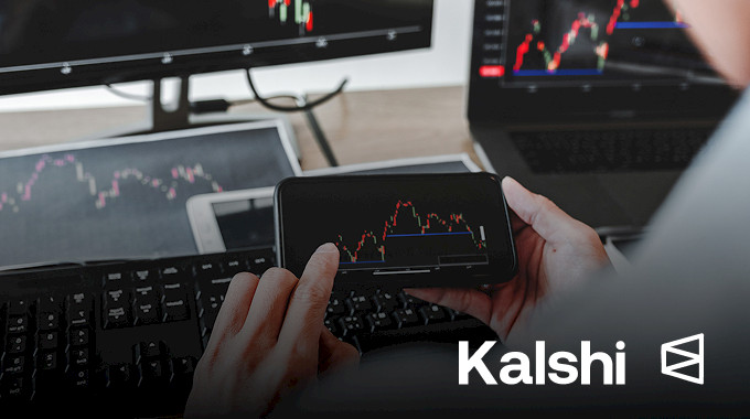 Hands hold a smartphone showing a market chart; Kalshi and Polymarket logos.